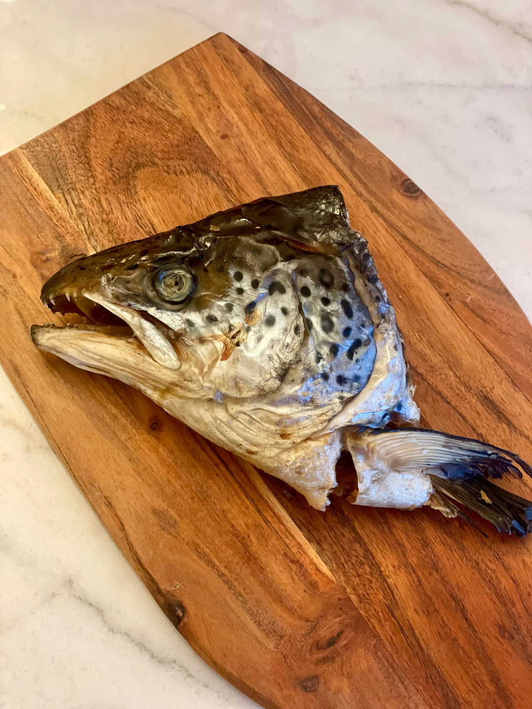 Image of a salmon head displayed on a wooden tray, showcasing the natural dog treat. The presentation highlights the freshness and quality of the salmon head, emphasizing its nutritional benefits as a high-protein snack for dogs.